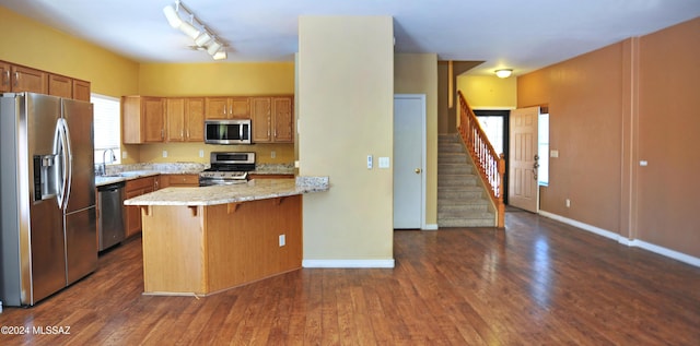 kitchen with light stone countertops, appliances with stainless steel finishes, dark hardwood / wood-style flooring, kitchen peninsula, and a kitchen breakfast bar