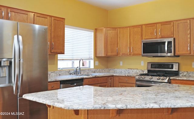 kitchen with kitchen peninsula, light stone countertops, sink, and appliances with stainless steel finishes