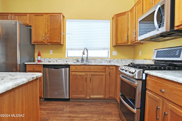 kitchen with light stone countertops, appliances with stainless steel finishes, dark wood-type flooring, and sink