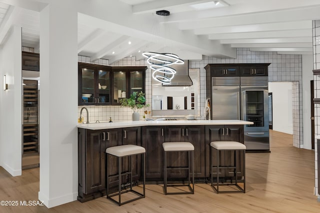 bar with tasteful backsplash, dark brown cabinets, high end fridge, light wood-type flooring, and lofted ceiling with beams