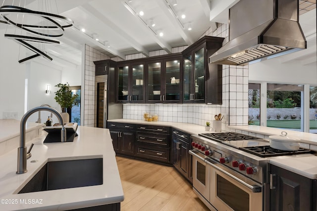 kitchen featuring wall chimney range hood, light wood-type flooring, sink, beam ceiling, and range with two ovens