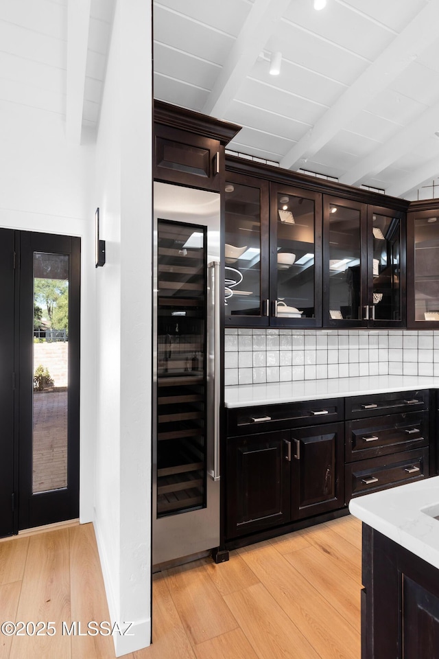 bar featuring dark brown cabinets, wine cooler, decorative backsplash, and light hardwood / wood-style flooring