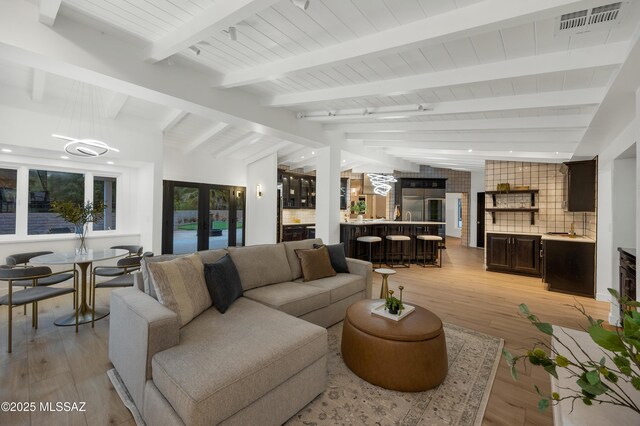 living room with light wood-type flooring, french doors, lofted ceiling with beams, and bar area