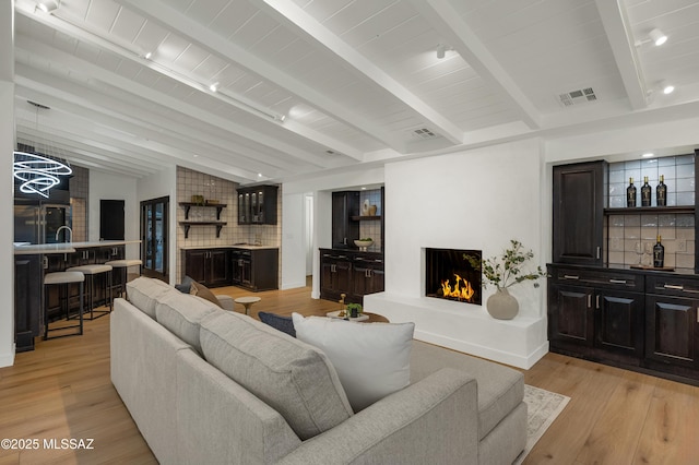 living room with a fireplace, lofted ceiling with beams, wooden ceiling, bar area, and light hardwood / wood-style flooring