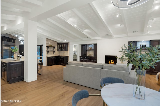 living room featuring sink, light hardwood / wood-style floors, lofted ceiling with beams, and a large fireplace