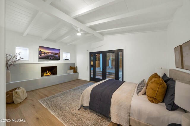 bedroom featuring french doors, access to exterior, lofted ceiling with beams, hardwood / wood-style flooring, and a tile fireplace