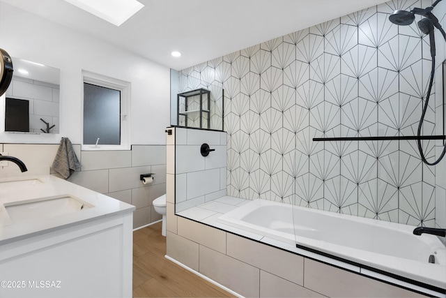 full bathroom with hardwood / wood-style floors, tile walls, vanity, tiled shower / bath, and toilet