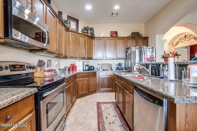 kitchen featuring stainless steel appliances, light stone counters, a center island with sink, and sink