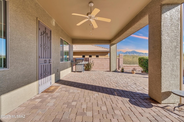 patio terrace at dusk with a mountain view, grilling area, and ceiling fan