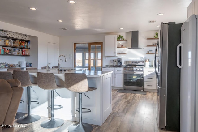 kitchen with stainless steel appliances, white cabinetry, a kitchen breakfast bar, light countertops, and wall chimney exhaust hood