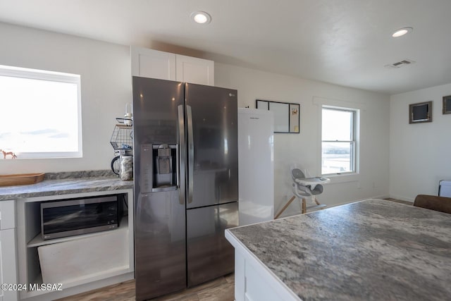 kitchen with recessed lighting, white cabinets, dark stone countertops, and black fridge