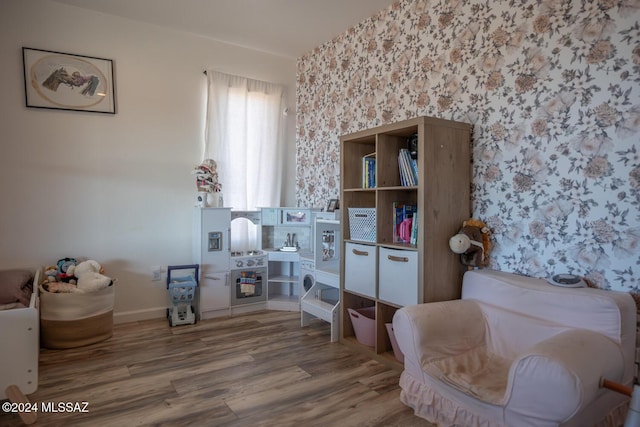 living area featuring an accent wall, wood finished floors, wallpapered walls, and baseboards
