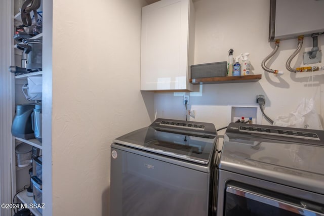 washroom featuring water heater, separate washer and dryer, and cabinet space