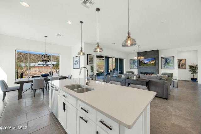 kitchen featuring a large fireplace, sink, a center island with sink, white cabinets, and hanging light fixtures