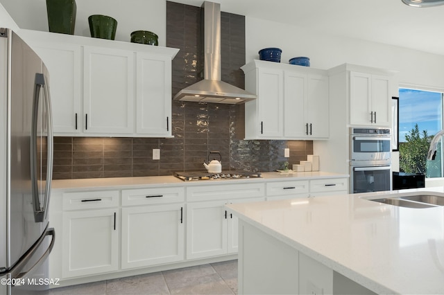 kitchen featuring appliances with stainless steel finishes, backsplash, white cabinetry, and wall chimney range hood