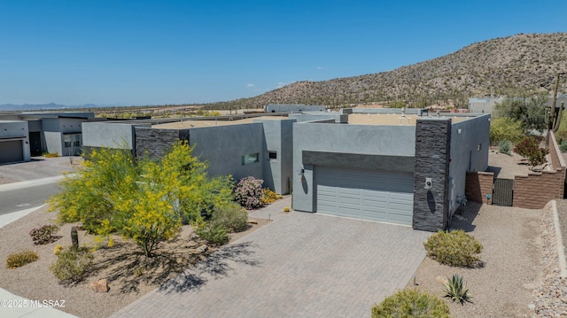 view of front of house with stucco siding, an attached garage, a mountain view, and decorative driveway