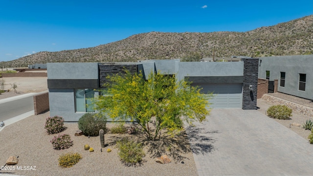 view of front of home with stucco siding, an attached garage, a mountain view, and decorative driveway
