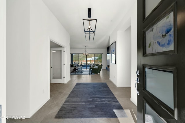 hall featuring baseboards, tile patterned floors, and a chandelier