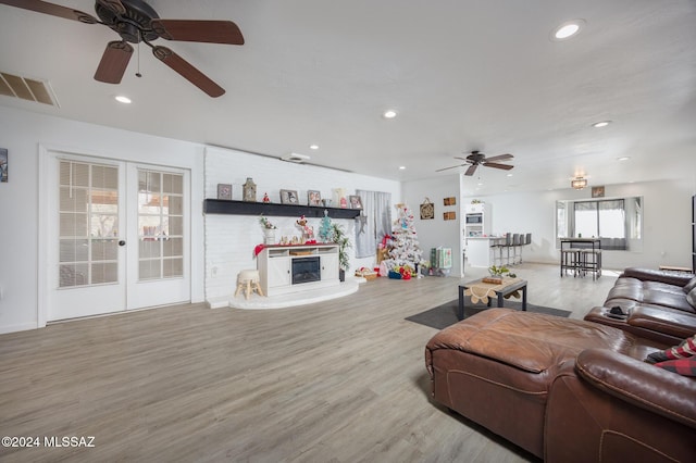 living room with ceiling fan, a large fireplace, and light wood-type flooring