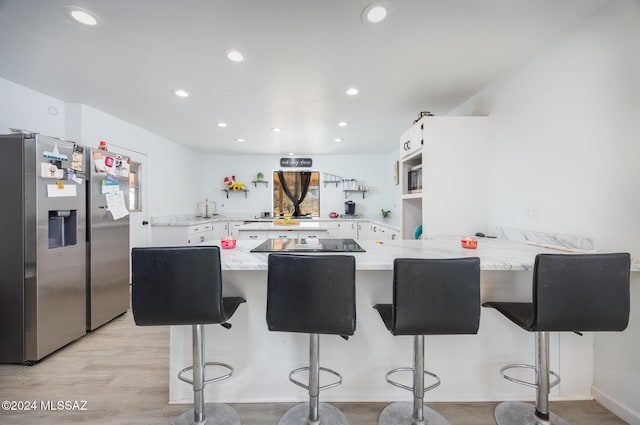 kitchen featuring a breakfast bar, white cabinets, stainless steel fridge, light stone countertops, and kitchen peninsula