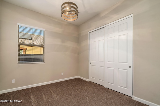 unfurnished bedroom featuring a closet, dark carpet, and an inviting chandelier