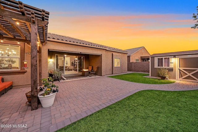 back house at dusk with a pergola, a patio area, and a lawn