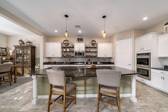 kitchen featuring an island with sink, stainless steel appliances, and decorative light fixtures