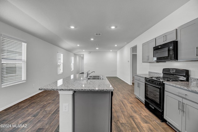 kitchen featuring black appliances, a center island with sink, sink, dark hardwood / wood-style floors, and light stone counters