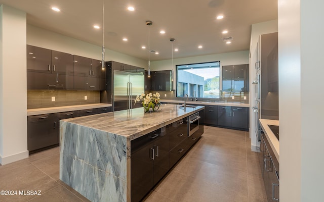 kitchen featuring pendant lighting, appliances with stainless steel finishes, a kitchen island, sink, and backsplash