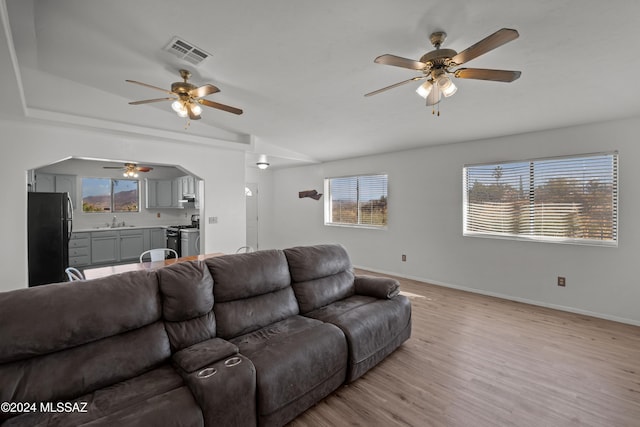 living room with light hardwood / wood-style floors, vaulted ceiling, ceiling fan, and sink