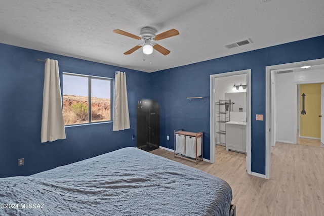 bedroom with a textured ceiling, ceiling fan, ensuite bathroom, and light hardwood / wood-style flooring