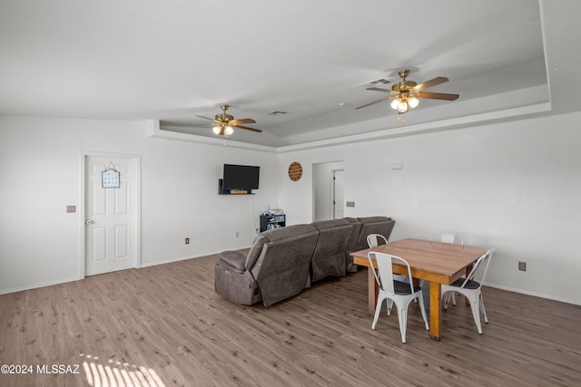 dining room with a tray ceiling, light hardwood / wood-style flooring, and ceiling fan