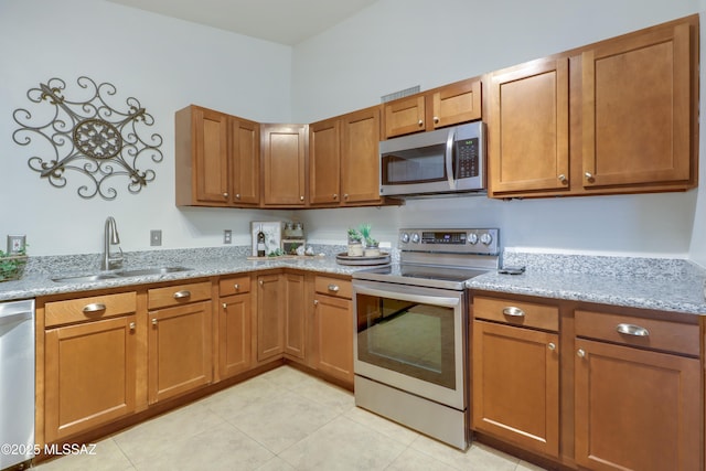 kitchen featuring light stone counters, sink, light tile patterned floors, and stainless steel appliances