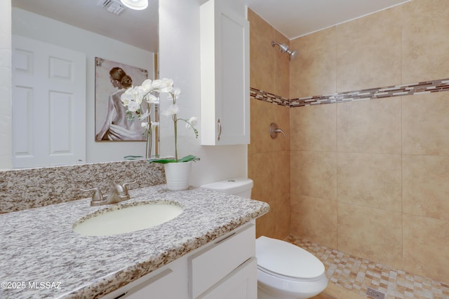 bathroom featuring a tile shower, vanity, and toilet