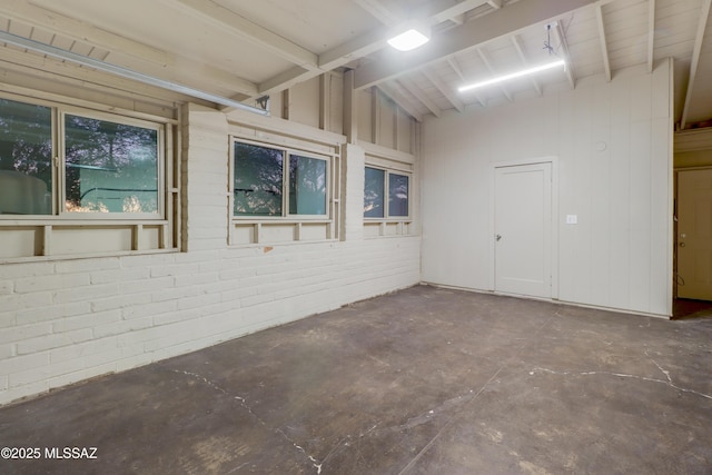 empty room with vaulted ceiling and brick wall