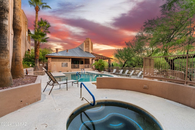 pool at dusk with a hot tub and a patio area