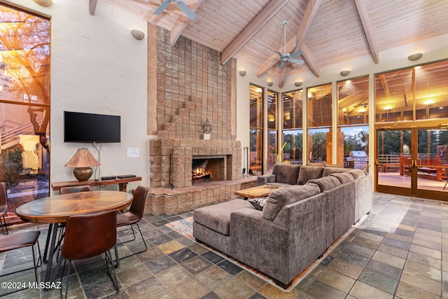 living room with a stone fireplace, ceiling fan, beamed ceiling, and high vaulted ceiling