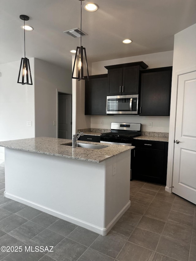 kitchen with pendant lighting, sink, a kitchen island with sink, stainless steel appliances, and light stone countertops