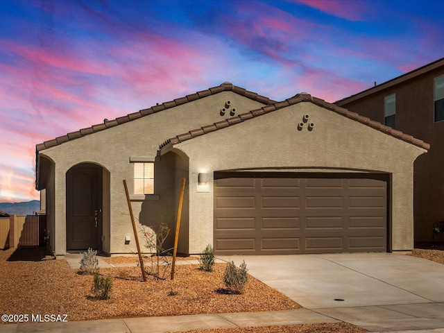 mediterranean / spanish-style home with a garage, concrete driveway, a tile roof, and stucco siding