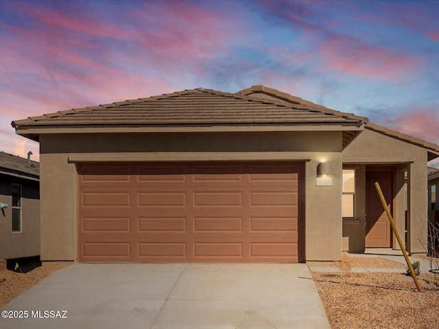 view of front facade with stucco siding, concrete driveway, a tile roof, and an attached garage