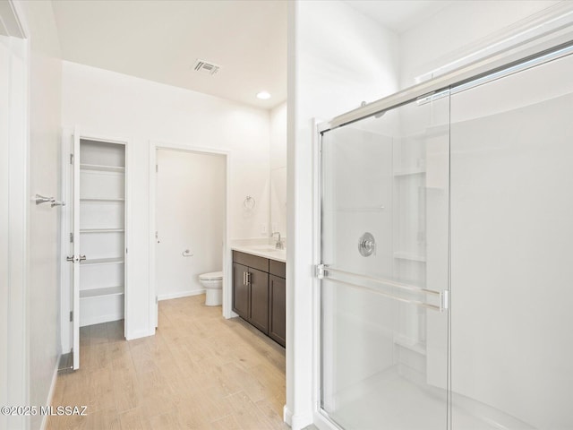 bathroom with visible vents, toilet, wood finished floors, vanity, and a shower stall