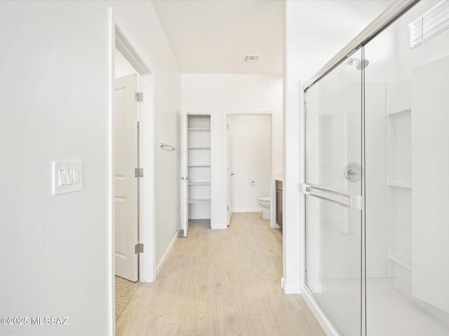 full bathroom with toilet, wood finished floors, visible vents, a spacious closet, and a stall shower