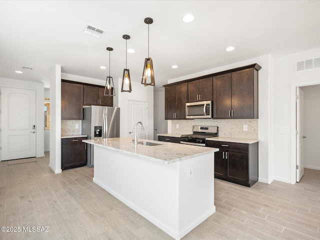 kitchen with visible vents, appliances with stainless steel finishes, a kitchen island with sink, dark brown cabinets, and a sink