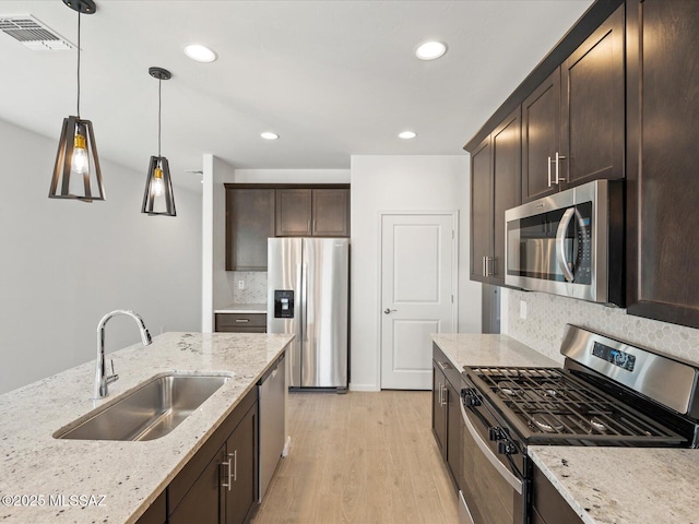 kitchen with visible vents, light stone counters, stainless steel appliances, pendant lighting, and a sink