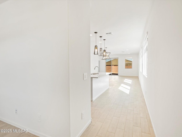 corridor with light wood-style floors, visible vents, a sink, and baseboards