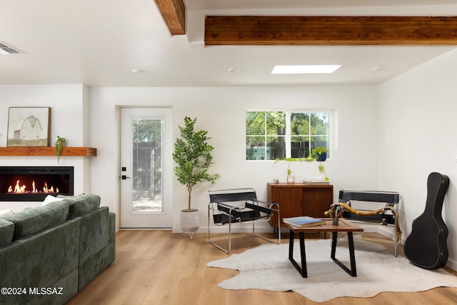 living area featuring baseboards, visible vents, wood finished floors, a lit fireplace, and beam ceiling