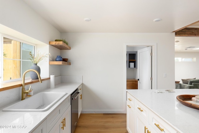 kitchen featuring light wood-style flooring, a sink, light countertops, stainless steel dishwasher, and open shelves