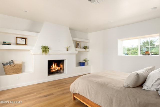 bedroom with baseboards, a fireplace, visible vents, and wood finished floors