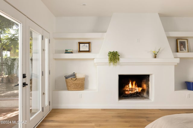 interior space featuring a large fireplace, built in shelves, wood finished floors, and french doors