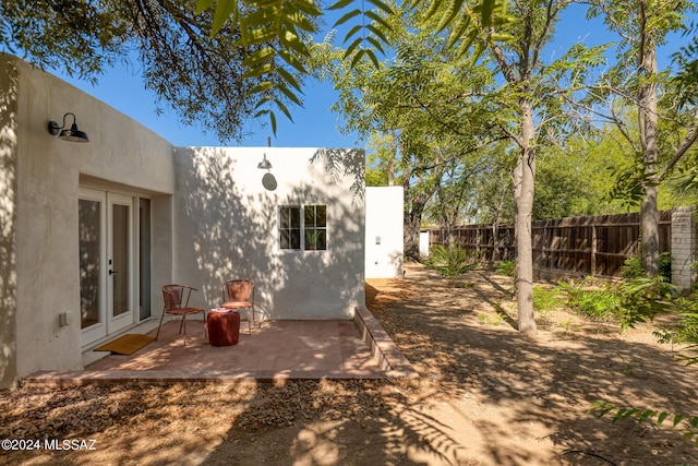 rear view of house with french doors, a patio area, fence, and stucco siding